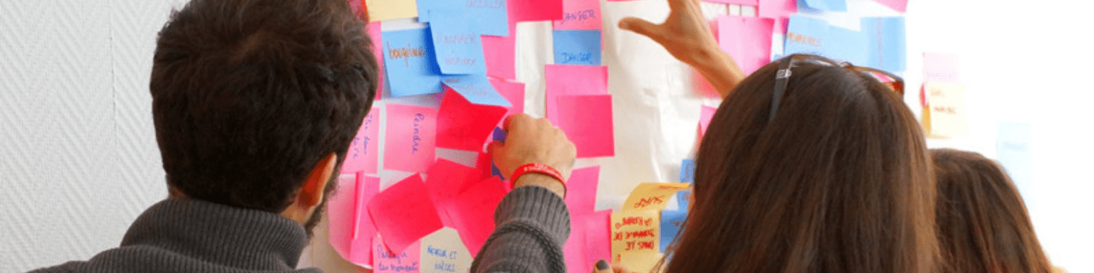 3 personnes de dos qui collent des post its sur un mur