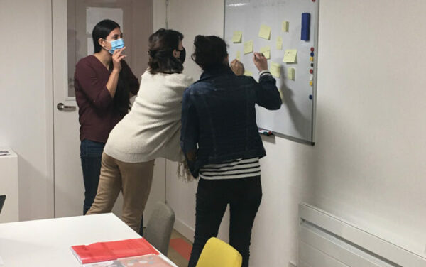 3 personnes debout collent des posts sur un tableau