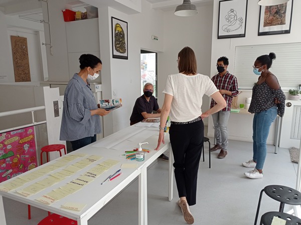 Photo lors d'un atelier collaboratif. 4 personnes sont debout et une personne assise. Des posts it sont sur la table